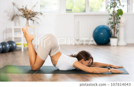 Young woman yoga trainer performing chest-stand pose on black rug Young woman yoga trainer performing chest-stand pose on black rug 107814043
