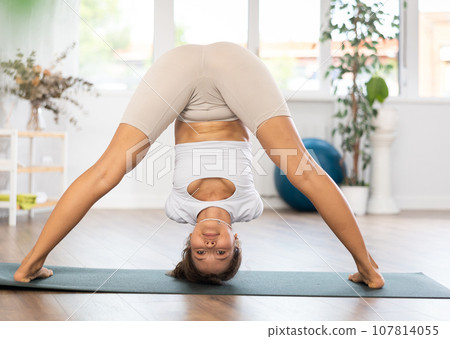 Young woman yoga trainer performing forward bend pose on black rug 107814055