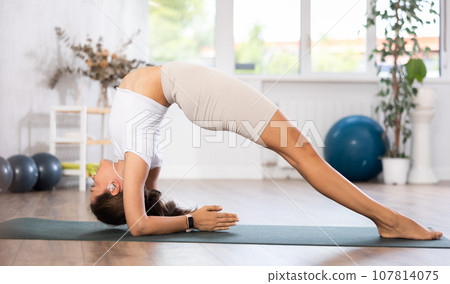 Young woman yoga trainer performing forearm stand pose on black rug 107814075