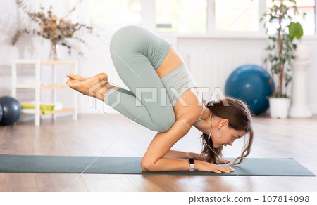 Young woman yoga trainer performing crow pose on black rug 107814098