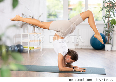 Young woman yoga trainer performing forearm stand pose on black rug Young woman yoga trainer performing forearm stand pose on black rug 107814099