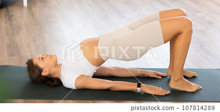 Experienced girl fitness club teacher performs setu bandha sarvangasana 107814289