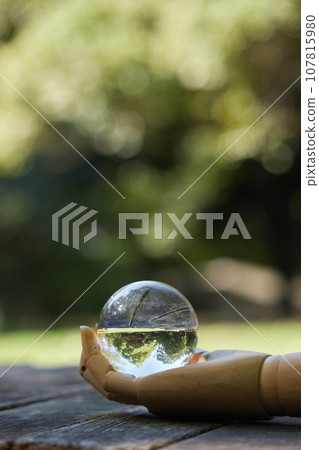 Scenery of one hand of a drawing doll and a transparent crystal glass ball on a table in the park Scenery of one hand of a drawing doll and a transparent crystal glass ball on a table in the park 107815980