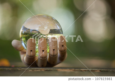Scenery of one hand of a drawing doll and a transparent crystal glass ball on a table in the park Scenery of one hand of a drawing doll and a transparent crystal glass ball on a table in the park 107815981
