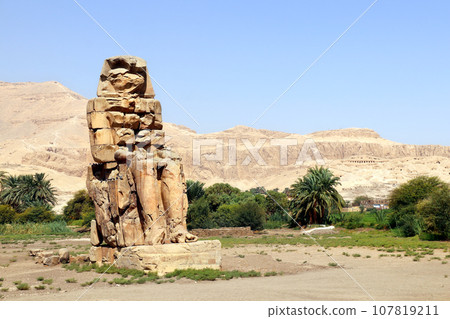 One of the famous Colossi of Memnon, Valley of Kings, Luxor, Egypt. Ancient stone statue of Pharaoh Amenhotep III in Theban Necropolis 107819211