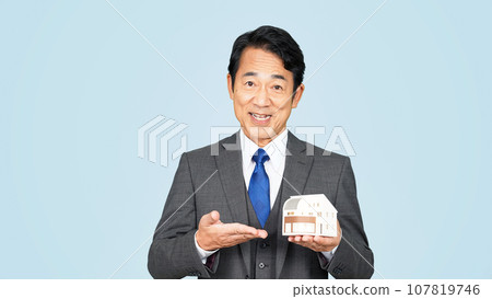 Middle-aged businessman showing a house model Middle-aged businessman showing a house model 107819746