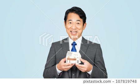 Middle-aged businessman showing a house model 107819748