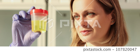 Concentrated woman looks at urine sample in container 107820047
