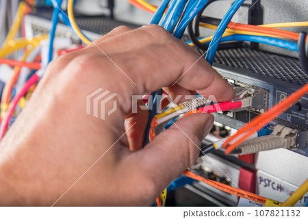 closeup of hand of administrator connecting network cable into switch 107821132