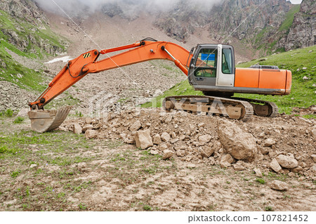 Excavator works in the highlands. Clears the consequences of a mudslide in the gorge of the mountains. repair and expansion of a road 107821452