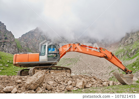 Excavator works in the highlands. Clears the consequences of a mudslide in the gorge of the mountains. repair and expansion of a road 107821455