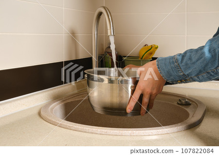 woman draws water from the tap into a saucepan 107822084