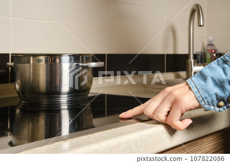 Unrecognizable woman turns on electric stove with touch control Unrecognizable woman turns on electric stove with touch control 107822086