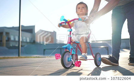 father teaches son baby to ride a children bike. happy family kid dream concept. baby baby rides a bike dad helps. father's day concept. child playing lifestyle riding a bike outdoors father teaches son baby to ride a children bike. happy family kid dream concept. baby baby rides a bike dad helps. father's day concept. child playing lifestyle riding a bike outdoors 107822604