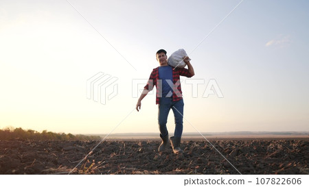 farmer working with sack in agricultural field. agriculture a business farm concept. farmer worker carries a bag with harvest at lifestyle sunset silhouette in agricultural field farmer working with sack in agricultural field. agriculture a business farm concept. farmer worker carries a bag with harvest at lifestyle sunset silhouette in agricultural field 107822606