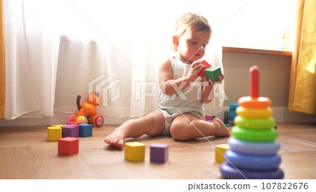 baby plays with toys cubes. kindergarten a teaching children kid dream concept lifestyle. baby on the floor of the house plays with a pyramid and cubes toys development of fine motor skills 107822676