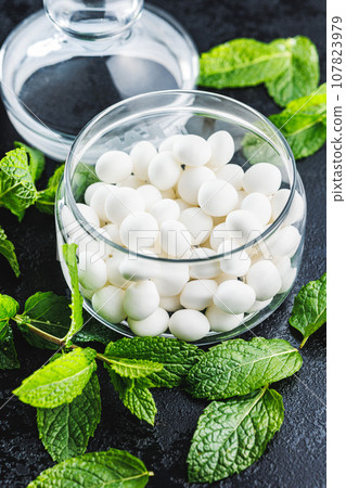 Mint candies in jar. Menthol bonbons and mint leaves on black table. 107823979