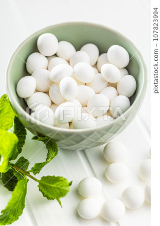 Mint candies in bowl. Menthol bonbons and mint leaves on white table. 107823994