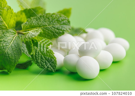 Mint candies. Menthol bonbons and mint leaves on green background. 107824010