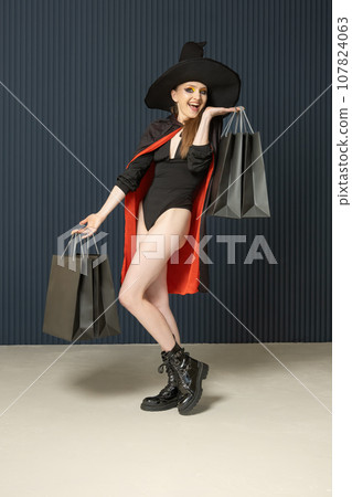 Full length portrait of young woman in black hat and coat with shopping bags . Halloween sale. Black Friday. Seasonal discounts Full length portrait of young woman in black hat and coat with shopping bags . Halloween sale. Black Friday. Seasonal discounts 107824063