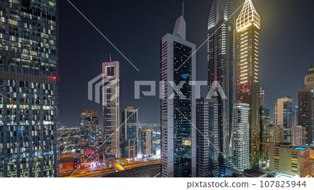 Panorama showing aerial view of Dubai International Financial District with many skyscrapers night timelapse. 107825944