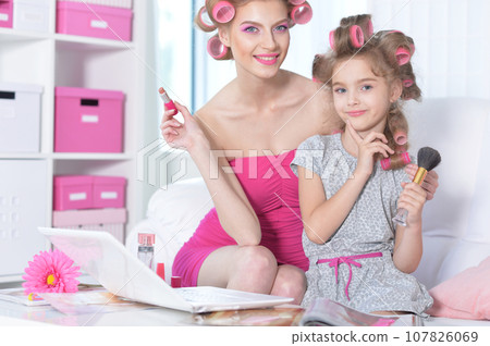 Mom and little daughter with hair curlers applying make up 107826069