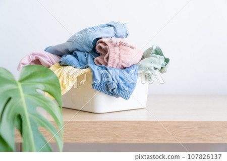 Selection of fresh unfolded laundry in white basket on wood table 107826137