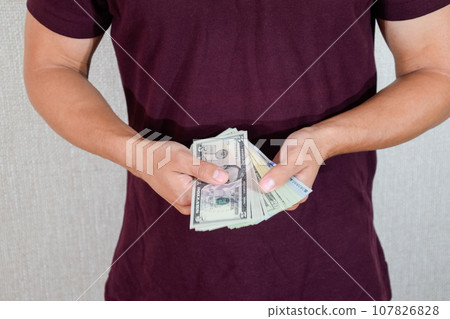 man holds a wad of dollars in his hands. US Dollars man holds a wad of dollars in his hands. US Dollars 107826828
