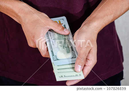 man holds a wad of dollars in his hands. US Dollars 107826839