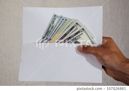 Money in white envelope in the hands of a man. Dollars, a wad of dollars. Money in white envelope in the hands of a man. Dollars, a wad of dollars. 107826861
