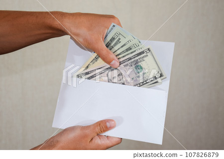 Money in white envelope in the hands of a man. Dollars, a wad of dollars. Money in white envelope in the hands of a man. Dollars, a wad of dollars. 107826879