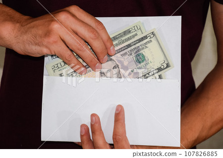 Money in white envelope in the hands of a man. Dollars, a wad of dollars. 107826885