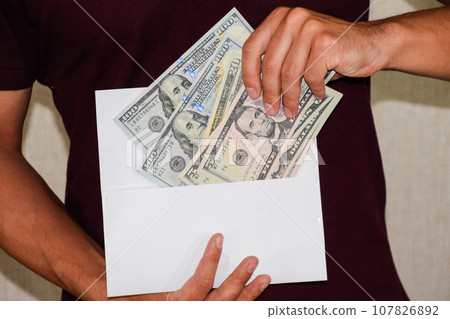 Money in white envelope in the hands of a man. Dollars, a wad of dollars. 107826892