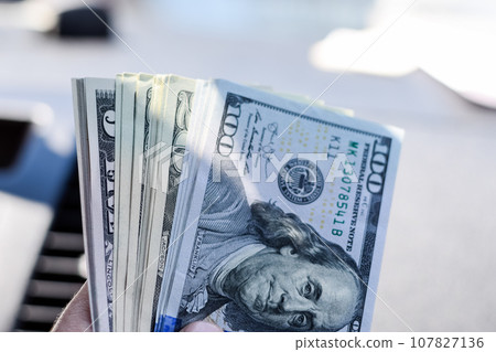 man hands over money in a car. A wad of dollars in his hand. 107827136