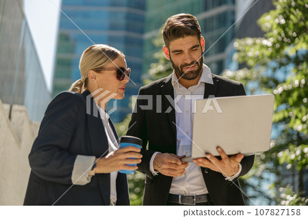 Contemporary businessman and businesswomen working outdoor on laptop with new startup project 107827158