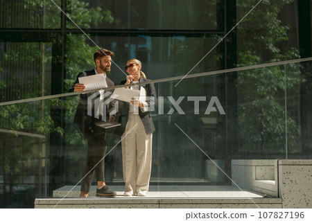 Business colleagues working with documents while standing on background of modern office building Business colleagues working with documents while standing on background of modern office building 107827196
