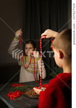 Two children make their own Christmas garlands of natural material 107827329