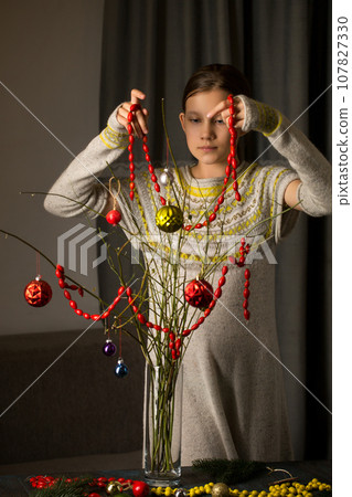 The girl decorates a bouquet of branches with an ecological garland of rose hips 107827330