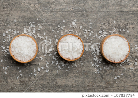 A wooden bowl of salt crystals on a wooden background. Salt in rustic bowls, top view with copy space A wooden bowl of salt crystals on a wooden background. Salt in rustic bowls, top view with copy space 107827784