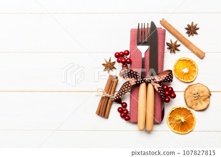 Top view of utensils on festive napkin on wooden background. Christmas decorations with dried fruits and cinnamon. New year dinner concept with copy space 107827815