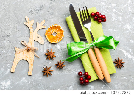 New year set of fork and knife on napkin. Top view of christmas decorations and reindeer on cement background. Close up of holiday family dinner concept 107827822