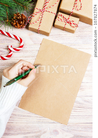 Female hands writing a letter to Santa Claus. Christmas gifts on a wooden background. View from above 107827874
