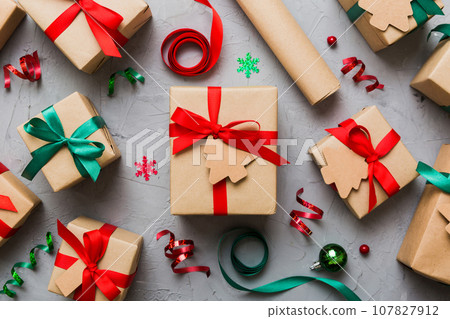 Woman is packing surprise gift for Christmas holidays, sitting at workplace with craft tools, top view. Woman wrapping Christmas gift at colored table Woman is packing surprise gift for Christmas holidays, sitting at workplace with craft tools, top view. Woman wrapping Christmas gift at colored table 107827912