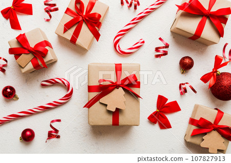 Woman is packing surprise gift for Christmas holidays, sitting at workplace with craft tools, top view. Woman wrapping Christmas gift at colored table Woman is packing surprise gift for Christmas holidays, sitting at workplace with craft tools, top view. Woman wrapping Christmas gift at colored table 107827913