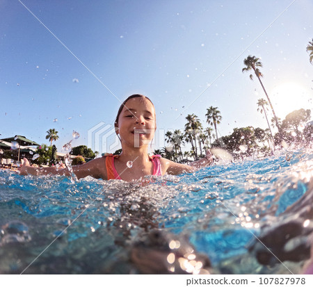 Little girl splashing water in the pool, playing in the water, having fun. Beach resort vacation by sea. Winter or summer seaside holiday. 107827978
