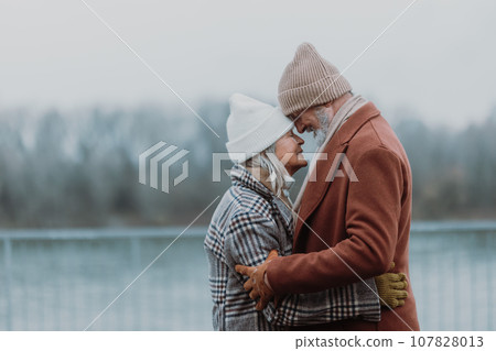 Elegant senior couple embracing near the river, during cold winter day. Elegant senior couple embracing near the river, during cold winter day. 107828013