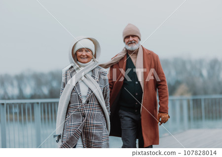 Elegant senior couple walking near the river, during cold winter day. 107828014
