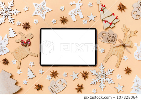 Festive decorations and toys on orange background. Top view of digital tablet. Merry Christmas concept 107828064