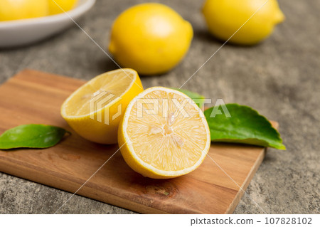 Top view with copy space for fresh and ripe lemons on cutting board. Healthy food background. Elegant background of lemon and lemon slices with squeezer colored background 107828102