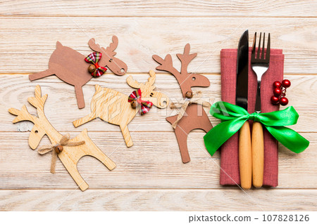 Top view of new year utensils on napkin with holiday decorations and reindeer on wooden background. Close up of christmas dinner concept 107828126
